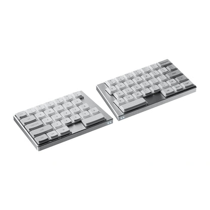 Angled studio shot of the silver ElimKeys Elytra split mechanical keyboard, featuring white low-profile keycaps with printed legends, separated on a pure white background.